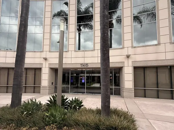 15615 Alton Parkway 的入口，一栋浅色石材办公楼，门牌号位于玻璃门上方，两侧种有棕榈树。
